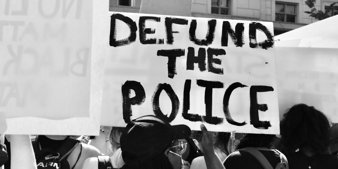 Ein Demonstrant hält bei einem Protest in zum Gedenken an George Floyd in 2020 ein Schild mit der Aufschrift "Defund the police" hoch.
